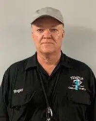 A man in black shirt and hat standing next to wall.