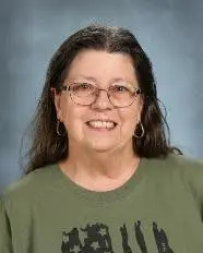 A woman with long hair and glasses is smiling.