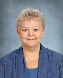 A woman with short hair and wearing blue is smiling.